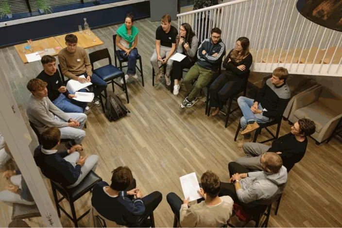 Des étudiants sont assis en cercle, échangeant leurs idées sur un sujet spécifique, avec des feuilles en main.