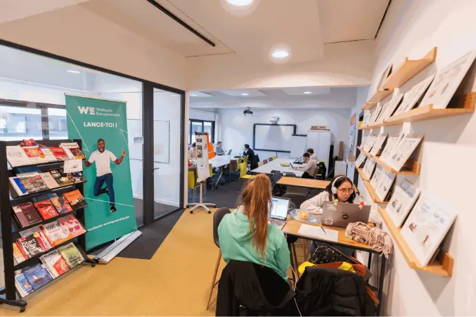 Des étudiants travaillent dans un grand espace, avec des tables hautes et des casques audio, créant un environnement d'étude collaboratif.
