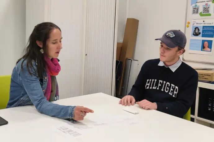 Une conseillère guide un étudiant attentif autour d’une table, soulignant des points importants sur une feuille.
