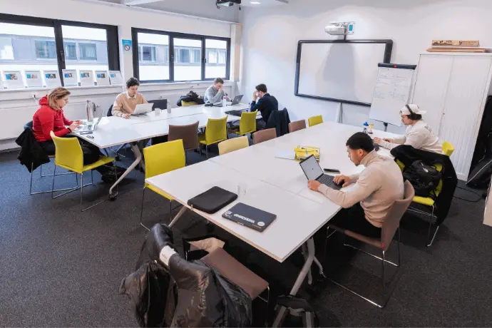 Un groupe d’étudiants travaille sur des ordinateurs, répartis autour de longues tables dans un espace de collaboration.